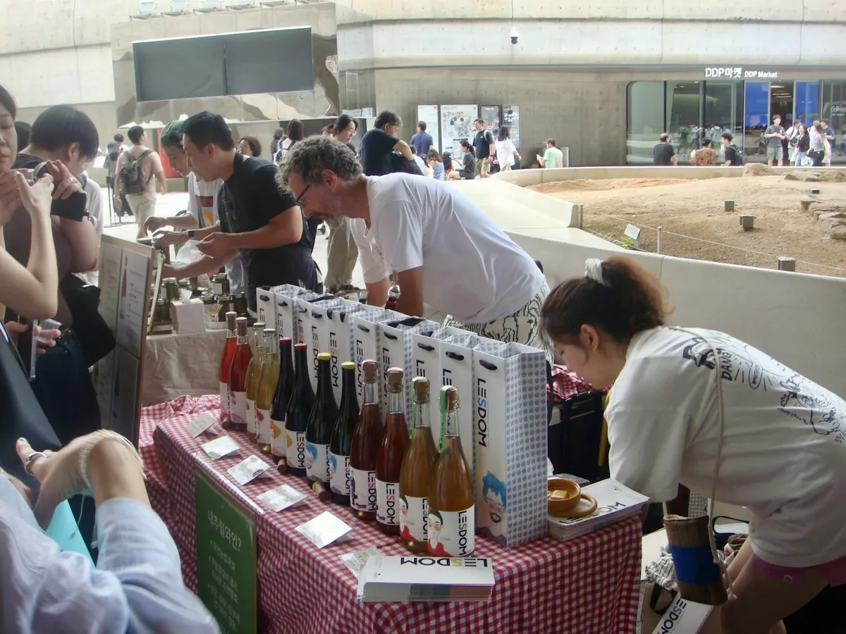 Puesto de degustación con botellas sobre una mesa y personas probando el producto.